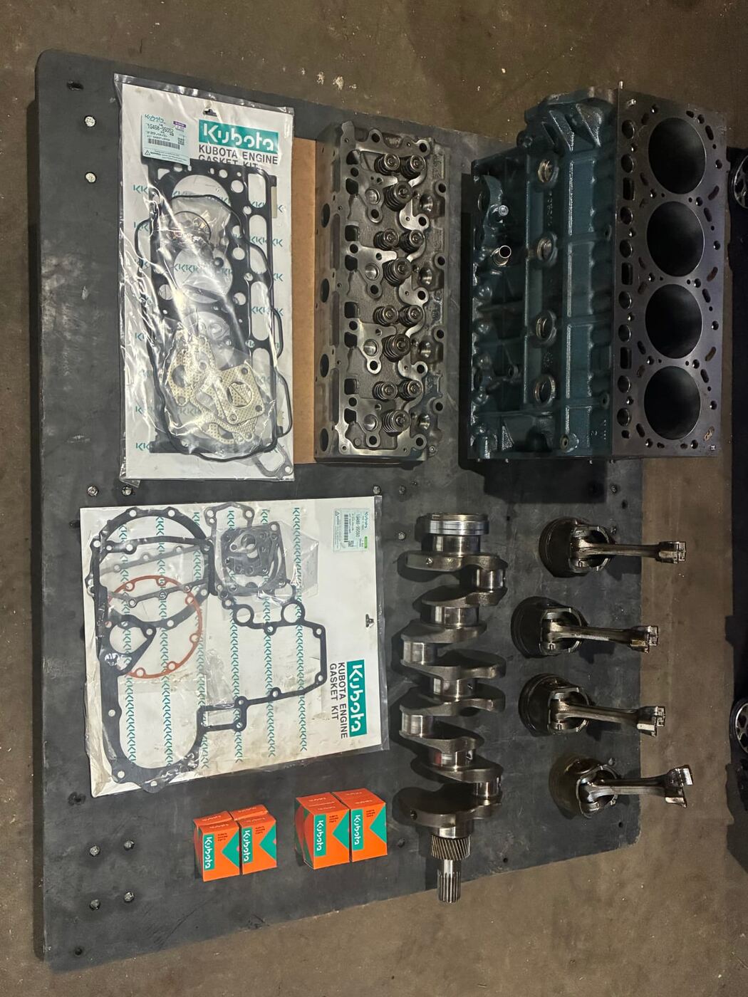 Kubota engine block, cylinder head, crankshaft, pistons, and genuine Kubota gasket kits laid out for a rebuild